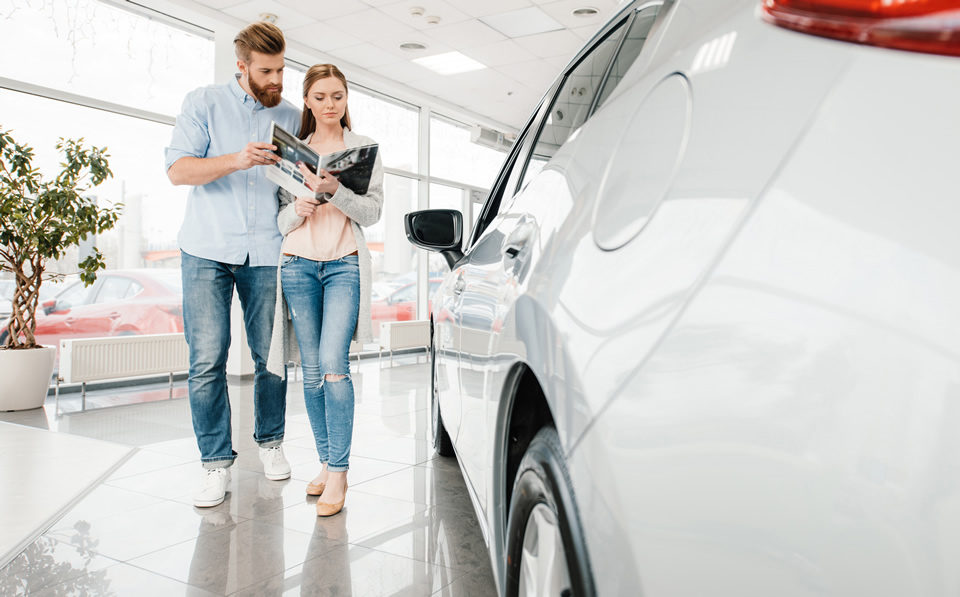 Couple reading pamphlet in a dealership, by a car
