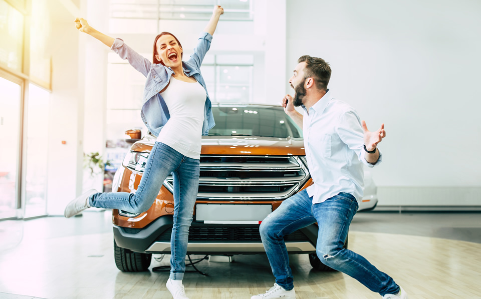 Couple cheering and jumping in front of new car