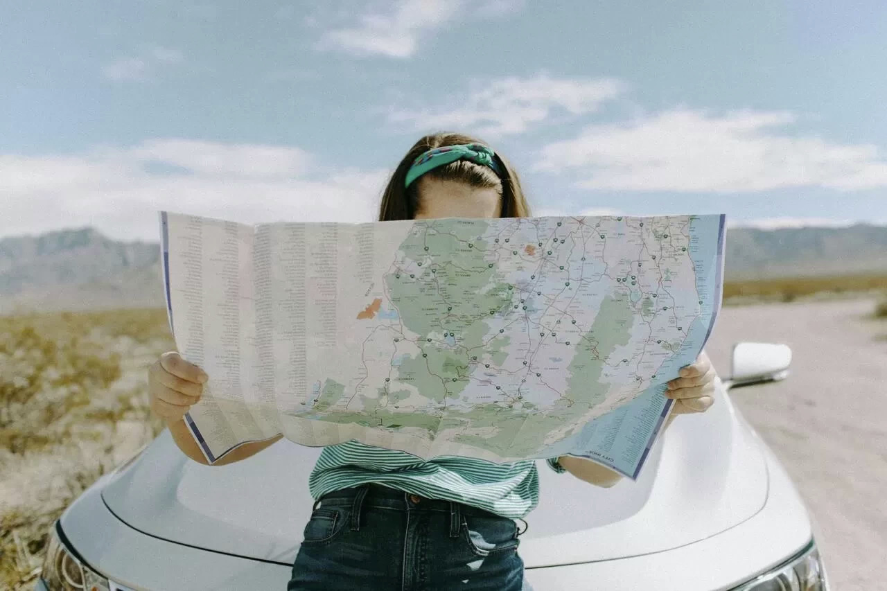 Picture of a woman looking at a map, leaning on the bonnet of a car